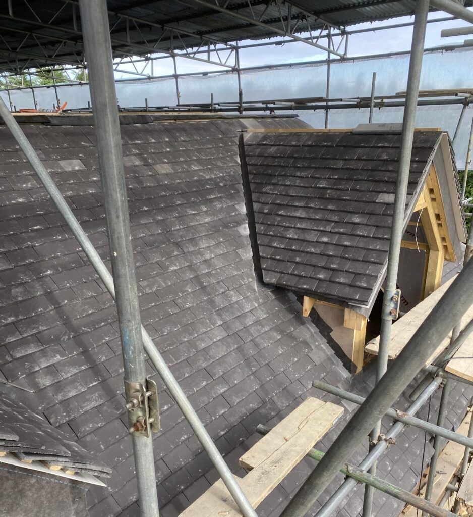 Dormer roof construction with slate tiles and scaffolding on residential property