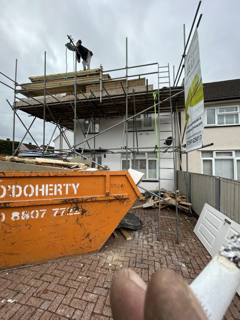 Loft conversion construction in progress with scaffolding, roofing work, and waste removal, showcasing a professionally managed building project.