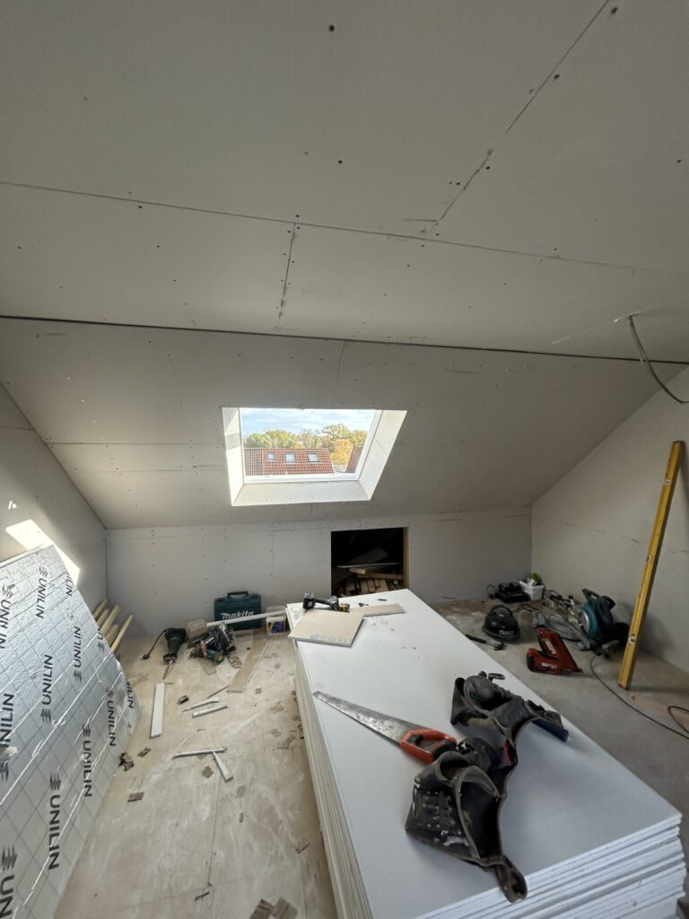 Loft conversion interior progressing with plasterboard installation, skylight fitting, and preparation for plastering and final finishing.