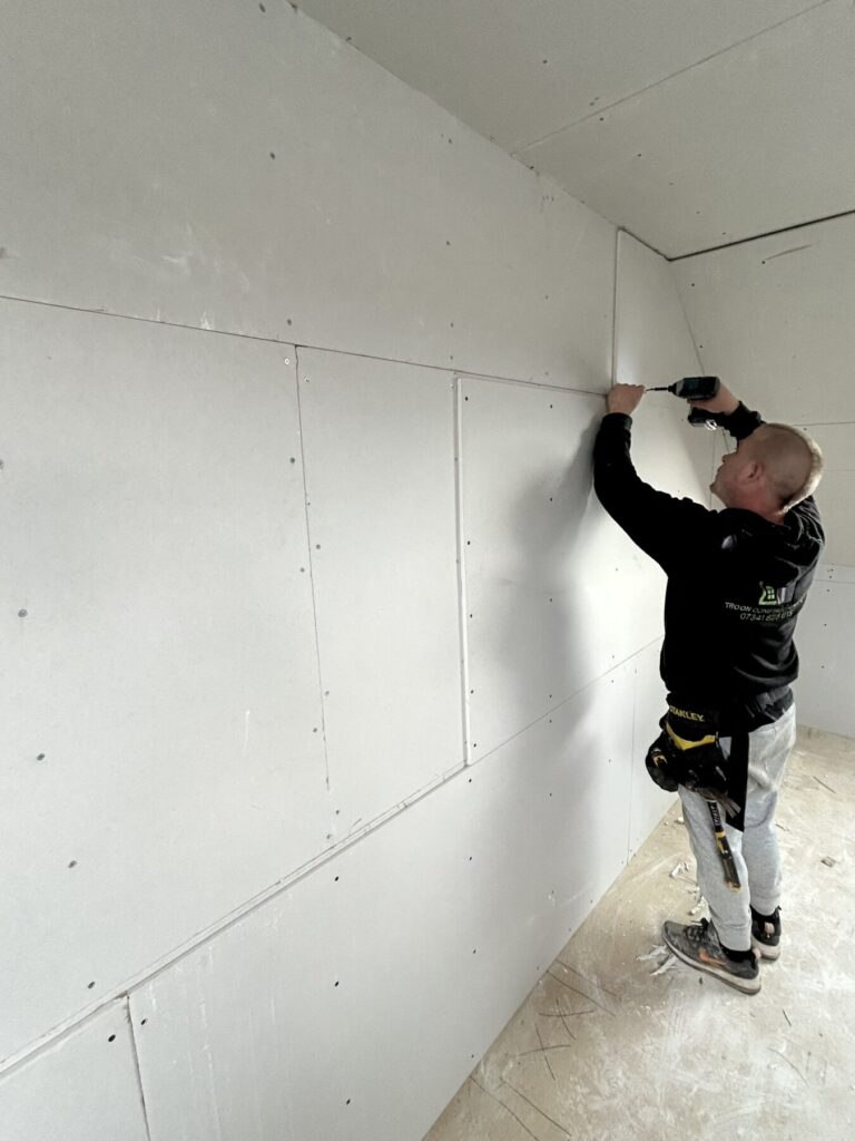 Internal loft conversion progress with plasterboard installation, creating smooth wall finishes ready for plastering and final decoration.