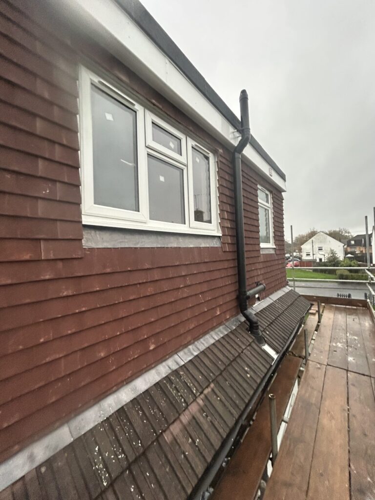 Dormer roof construction with timber cladding and scaffolding on residential property including gutter drain