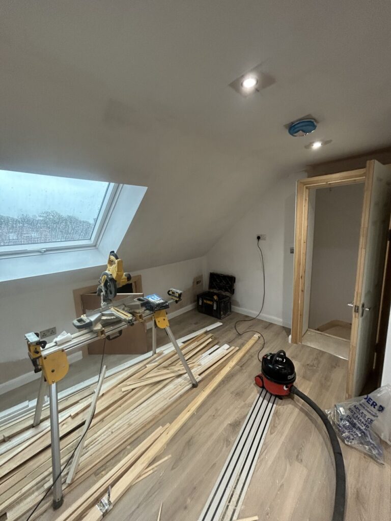 Loft room under construction with roof window, wooden flooring, power saw, and timber beams on the floor