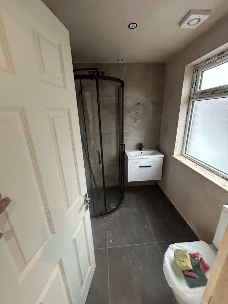 Modern bathroom with curved glass shower enclosure, wall-mounted sink unit, and grey floor tiles